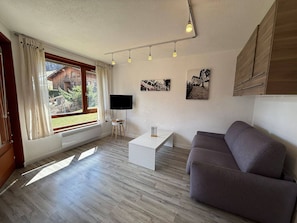 A modern living room with a grey sofa, a white coffee table, a flat-screen TV, and wooden flooring.