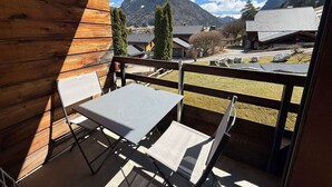 A balcony with a table and chairs, overlooking a mountain and a village.