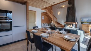 Una cocina moderna con electrodomésticos integrados, un comedor con mesa de madera para cuatro personas, y un espacio de sala acogedor con chimenea.