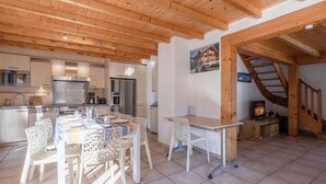 Una cocina moderna con electrodomésticos de acero inoxidable, un comedor con sillas blancas y una escalera de madera.