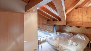 Un dormitorio de cabaña de madera con un altillo para dormir, techo de madera y ventana con vista a un balcón.