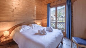 Una habitación de cabaña de madera con una cama, una silla y un ventanal con cortinas.