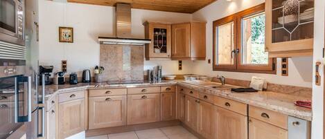 A spacious kitchen with wooden cabinets, a stainless steel refrigerator, and a large window providing natural light.