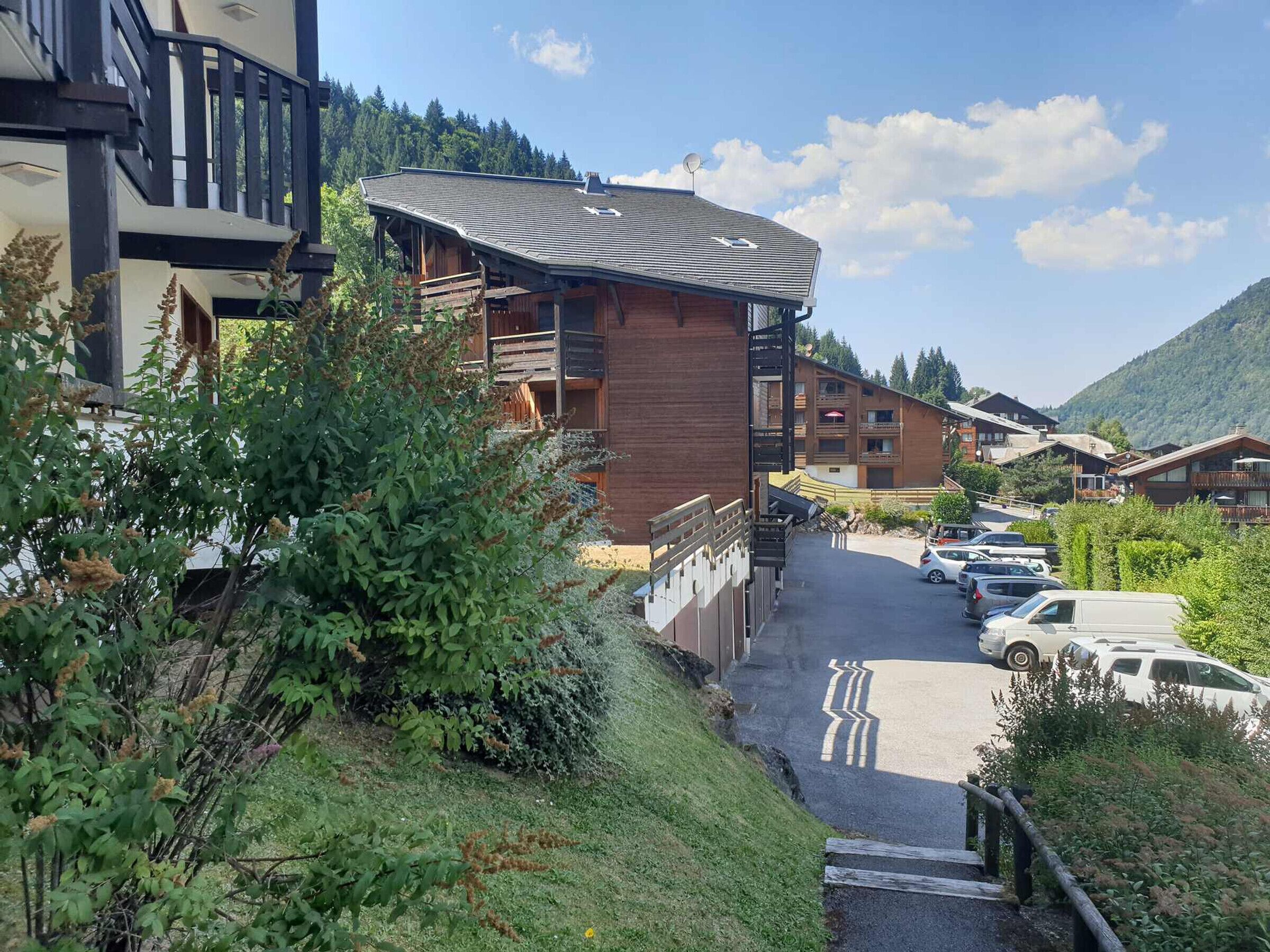 Una cabaña de montaña con techo curvo, balcones de madera y un estacionamiento con coches.