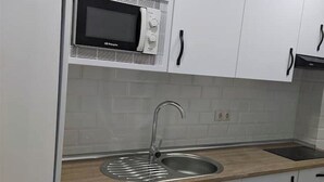 Una cocina funcional con armarios blancos, microondas, lavabo y lavadora.
