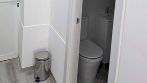 Un baño pequeño con paredes blancas, un inodoro y un bote de basura.