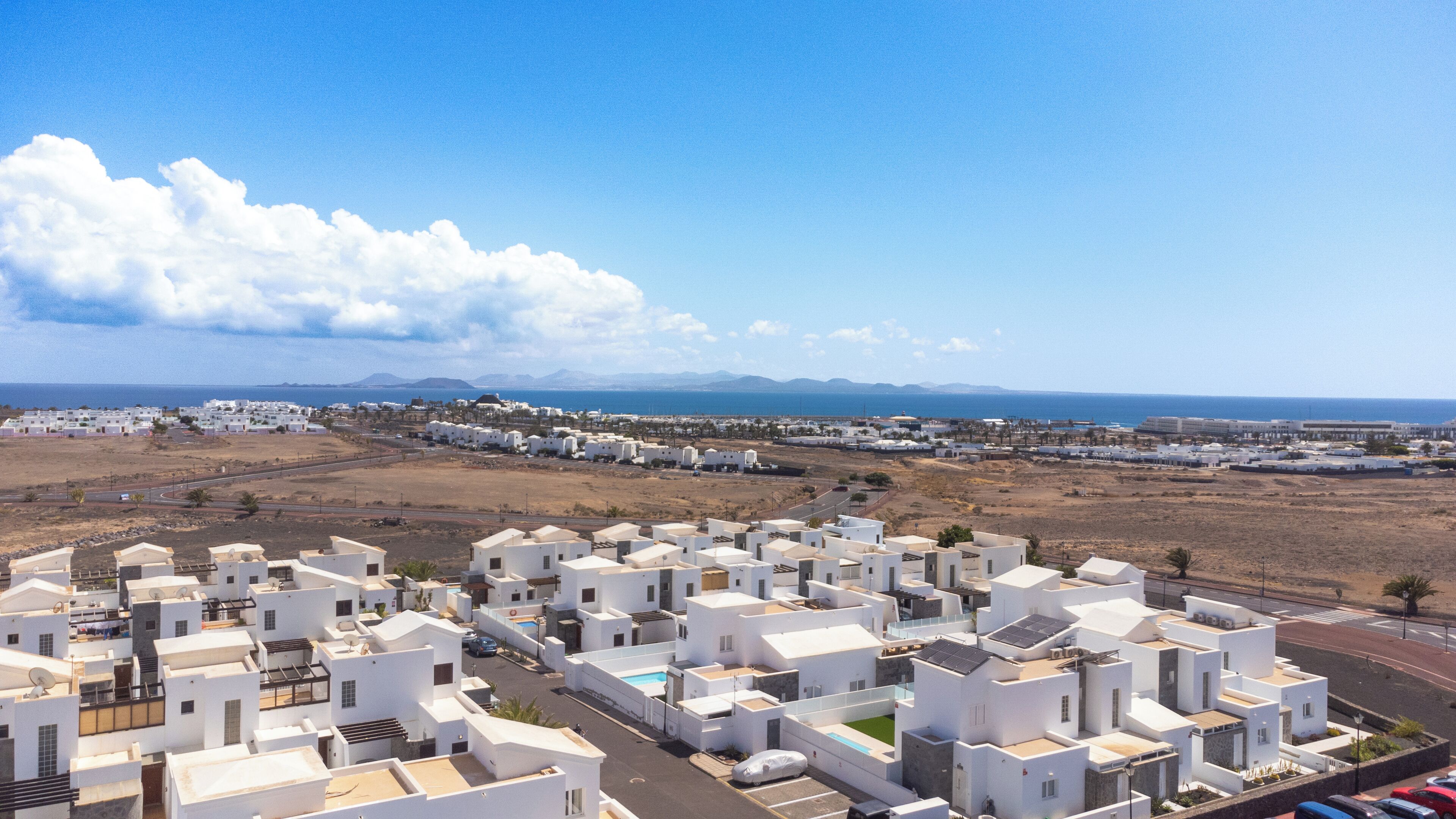 A coastal residential area with white buildings, a clear sky, and a view of the sea.