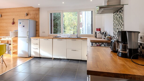 A modern kitchen with white cabinets, a wooden countertop, and a large window providing natural light.