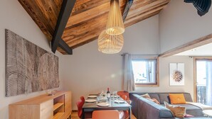 Un comedor moderno con techo de madera, un cuadro abstracto grande y un rincón de estar acogedor con sofá y cojines.