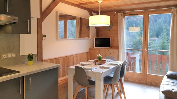 Cucina accogliente con travi in legno, zona pranzo con tavolo e sedie, e un'ampia finestra vista su spazi verdi.