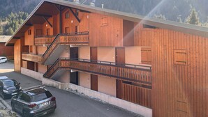 Un edificio in legno a due piani con balconi, una scala e un'area di parcheggio con auto.