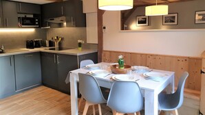 Una cucina moderna con mobili grigi, un piano di lavoro bianco e un'area pranzo con tavolo bianco e sedie blu.
