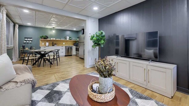 Una sala moderna con comedor, una cocina al fondo y un televisor de pantalla plana grande montado en la pared.
