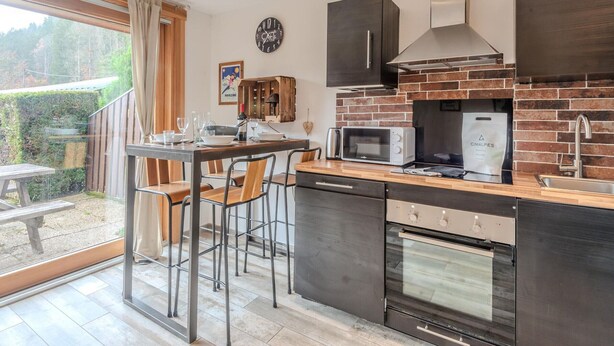 A modern kitchen with a brick backsplash, stainless steel appliances, and a dining area with bar stools. - Cosy T2 apartment with terrace 5 min from Avoriaz cable car (Morzine)