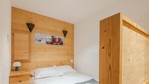 A bedroom with a wooden headboard, a bed with white linens, a gray blanket, and rolled towels. There is a wooden nightstand with a lamp and a small cabinet. - Cosy T2 apartment with terrace 5 min from Avoriaz cable car (Morzine)