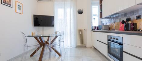 A modern kitchen with white cabinets, a built-in oven, and a dining area with a glass table and clear chairs.
