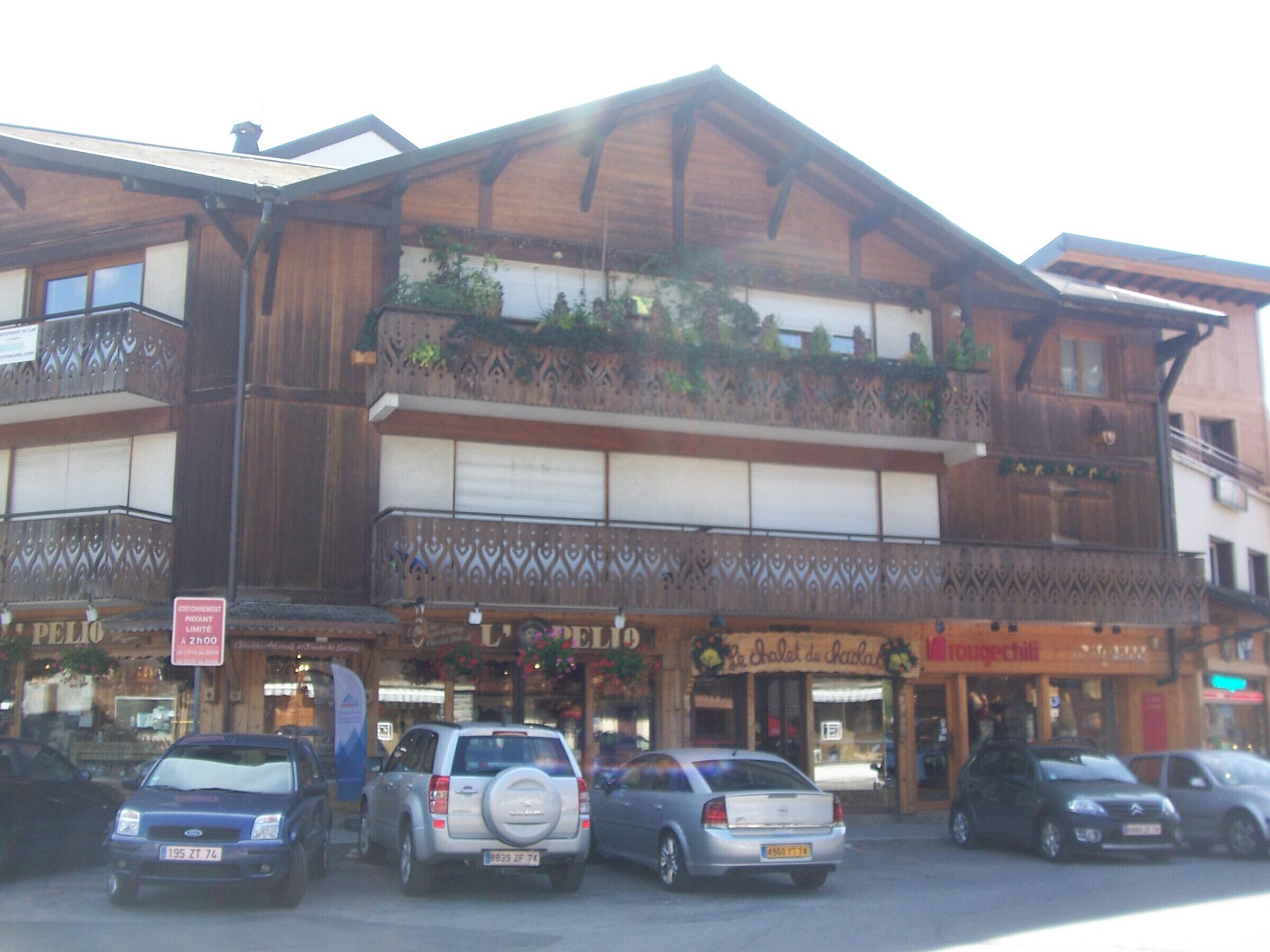 Ein mehrstöckiges Gebäude mit Holzfassade, bepflanzten Balkonen und verschiedenen Geschäften.