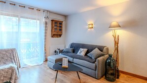 A cozy living room with a grey sofa, a small round table, and a lamp. There is a wooden cabinet on the wall and a window with curtains. - Renovated studio-cabin for 4, central Morzine, near slopes (Morzine)