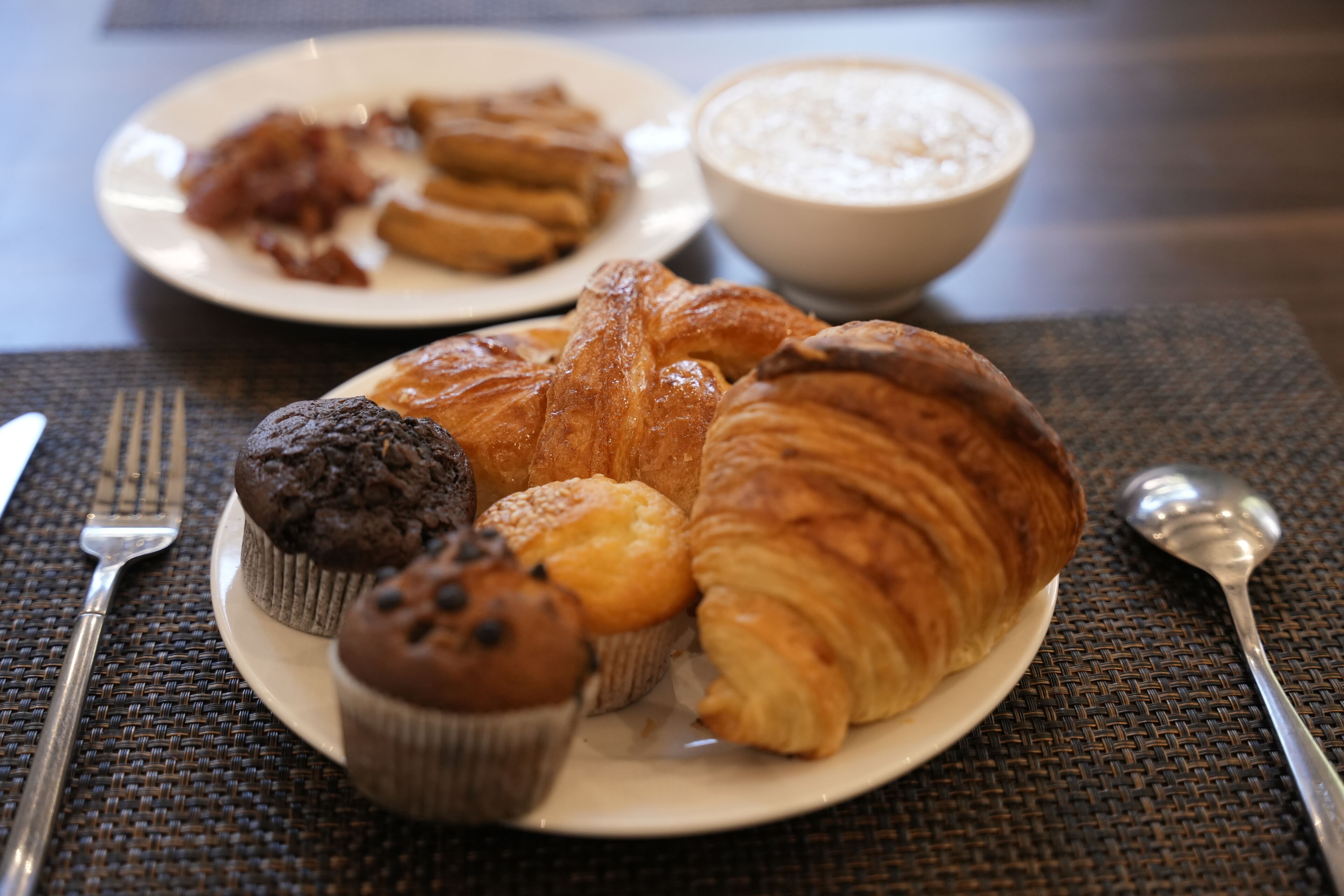 A breakfast plate with croissants, muffins, and a bowl of oatmeal.