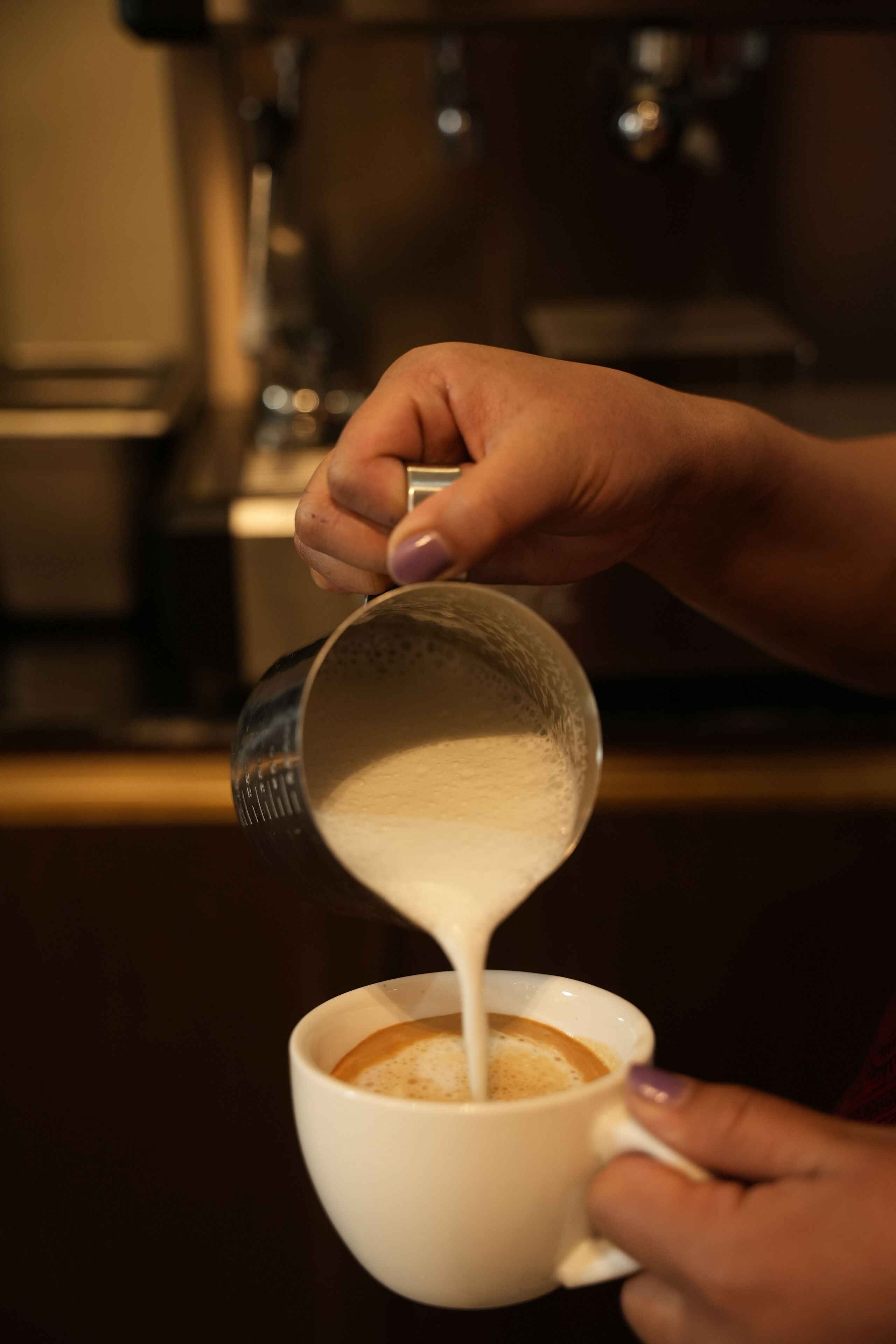 A hand pouring milk into a cup of coffee.