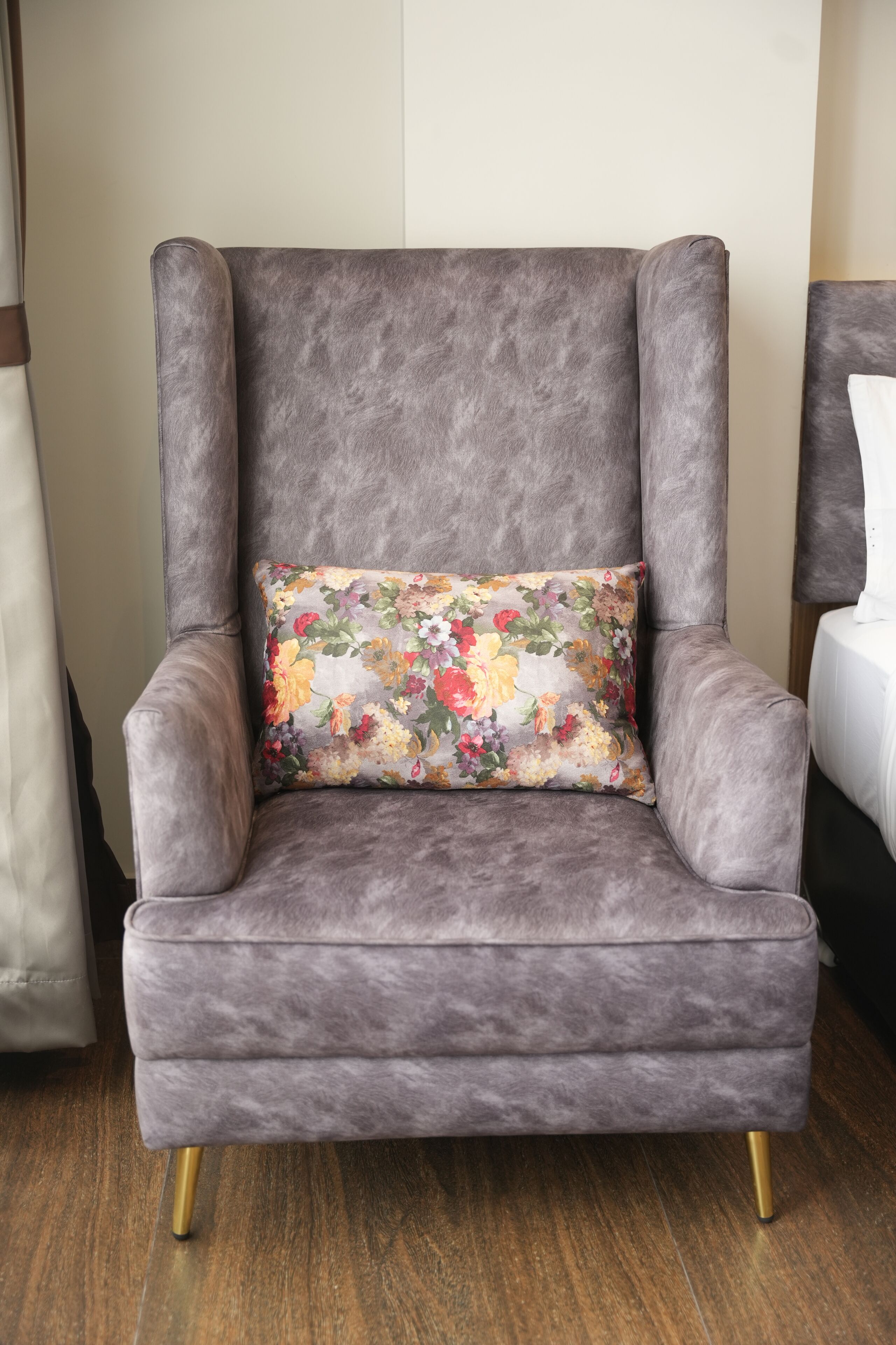 A grey upholstered armchair with a floral pillow, positioned on a wooden floor.