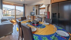 Comedor con mesa para cuatro, televisor y cocina moderna con refrigerador grande.