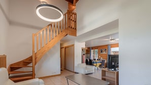 Amplia sala de estar con una escalera de madera, una mesa de comedor y una cocina visible a través de una puerta abierta.
