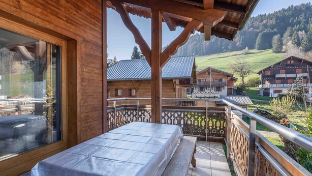 Un balcón de madera con una mesa y bancos, con vistas a un paisaje montañoso con casas de madera tradicionales.