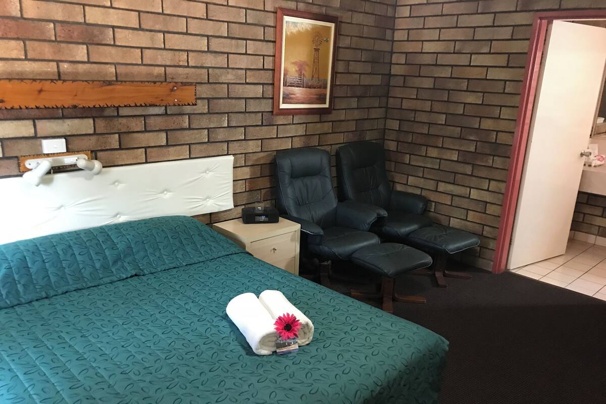 Ein Hotelzimmer mit Bett, Sessel, Nachttisch, einem Bild an der Wand und einer Tür.