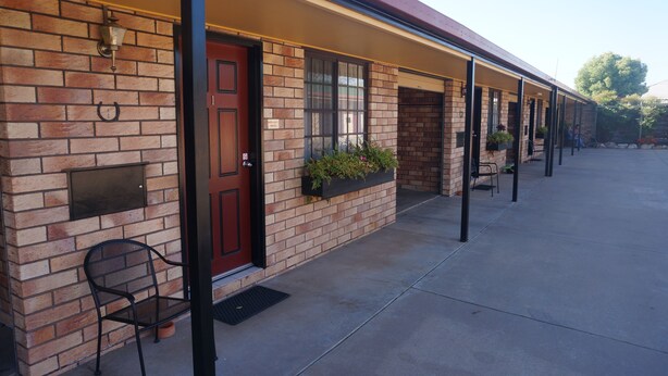 A row of motel rooms with brick walls, a red door, and outdoor seating. - Miles Outback Motel (Miles)