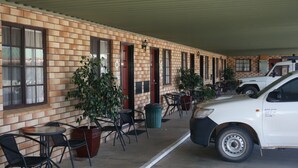 A brick building with a covered patio, outdoor seating, and a parked vehicle. - Miles Outback Motel (Miles)