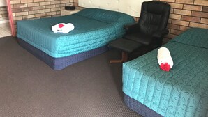 A room with two beds, a chair, a brick wall, and a framed picture. - Miles Outback Motel (Miles)