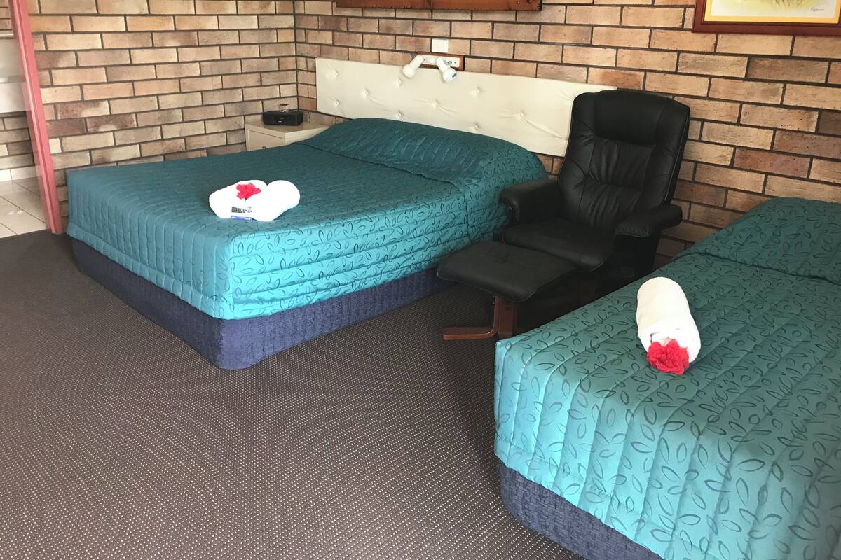 Ein Zimmer mit zwei Betten, einem Sessel, einer Ziegelwand und einem gerahmten Bild.