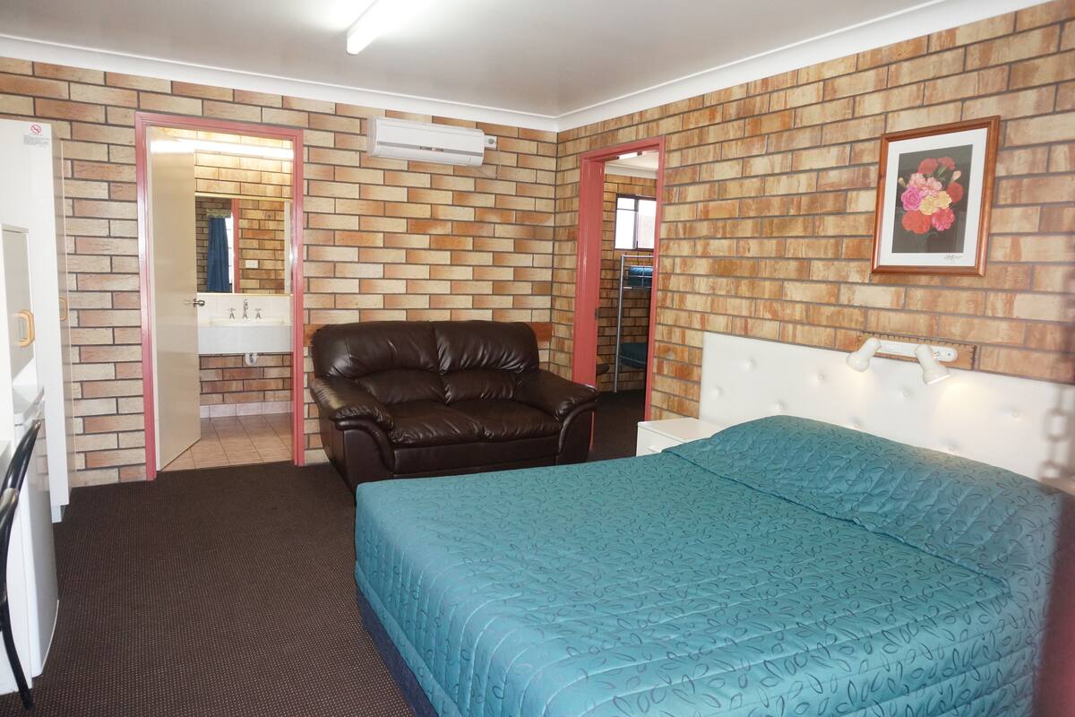 Ein Zimmer mit einer Ziegelwand, einem braunen Ledersofa, einer türkisblauen Bettdecke und einem gerahmten Blumenbild an der Wand.
