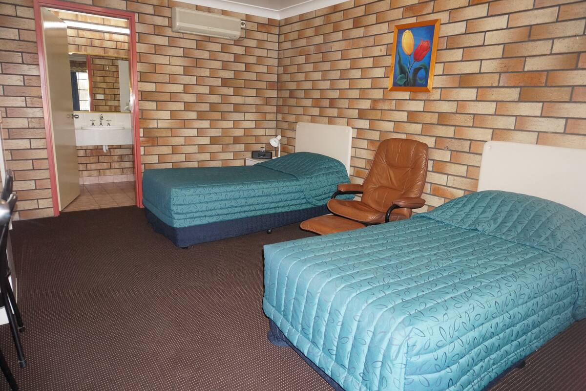 Ein Hotelzimmer mit zwei Betten, einem Schreibtisch, einem Stuhl, einem kleinen Tisch, einem Spiegel und einem Bild an der Wand.