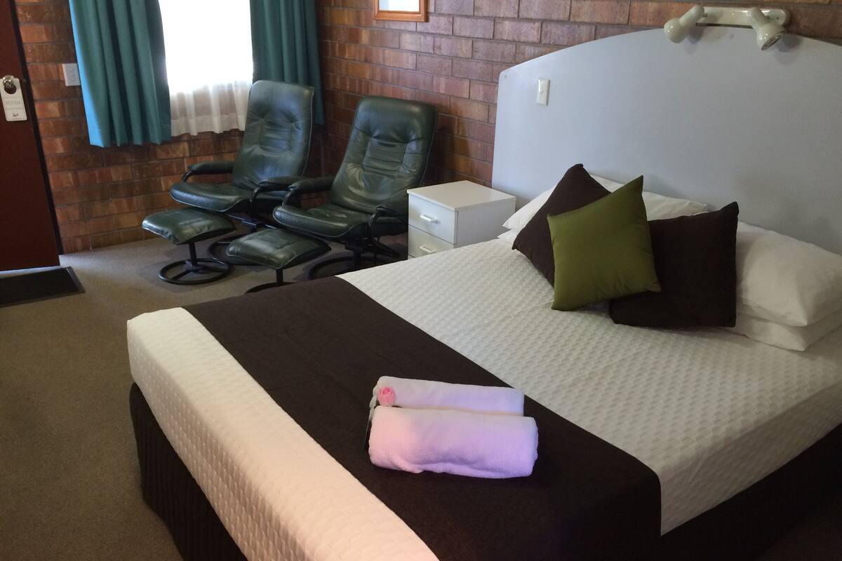 Ein Hotelzimmer mit einem großen Bett, zwei grünen Ledersesseln, einem kleinen weißen Nachttisch und einer Ziegelwand.
