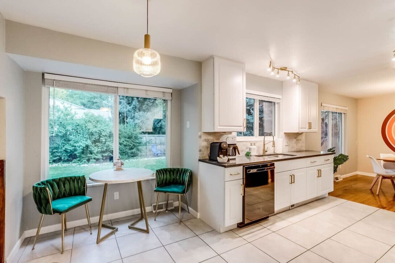 A modern kitchen with white cabinets, a central island, and a dining area with two green chairs.