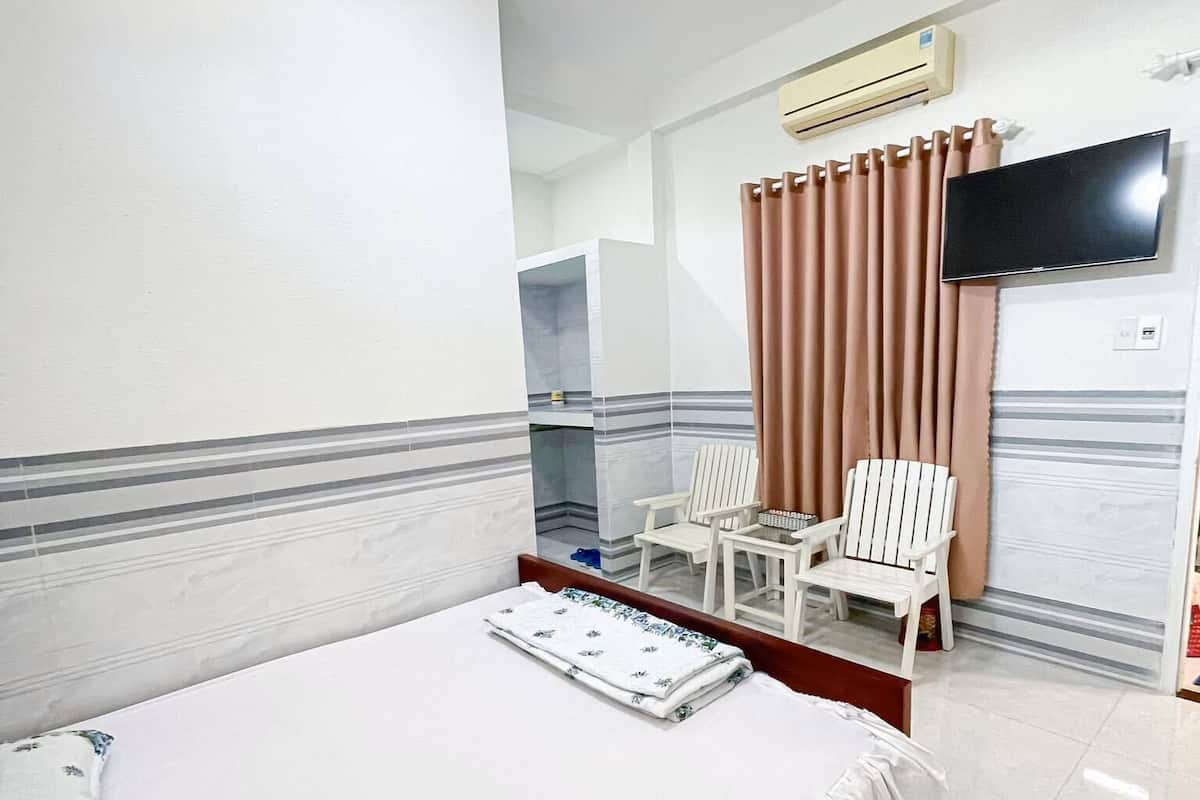 Une chambre d’hôtel avec un grand lit, un téléviseur fixé au mur et un coin salon avec deux fauteuils.