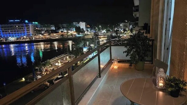 A balcony with a view of a cityscape at night, a table with a candle, and a potted plant. - Debbies apartment over the water! (Chalkida)