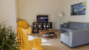 A living room with a sofa, a yellow armchair, a bookshelf, a TV, and a painting on the wall. - Debbies apartment over the water! (Chalkida)