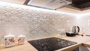 A modern kitchen with a black induction cooktop, white patterned backsplash, and wooden cabinets. - Debbies apartment over the water! (Chalkida)