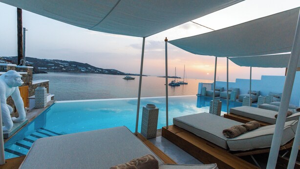 A poolside area with lounge chairs and a view of the sea at sunset. - Icon Mykonos (Mykonos)