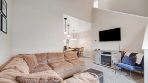 Een woonkamer met een grote beige hoekbank, een flatscreen televisie aan de wand en een open haard.