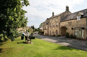 A traditional stone building with a pub sign, a bench, and a grassy area in front.