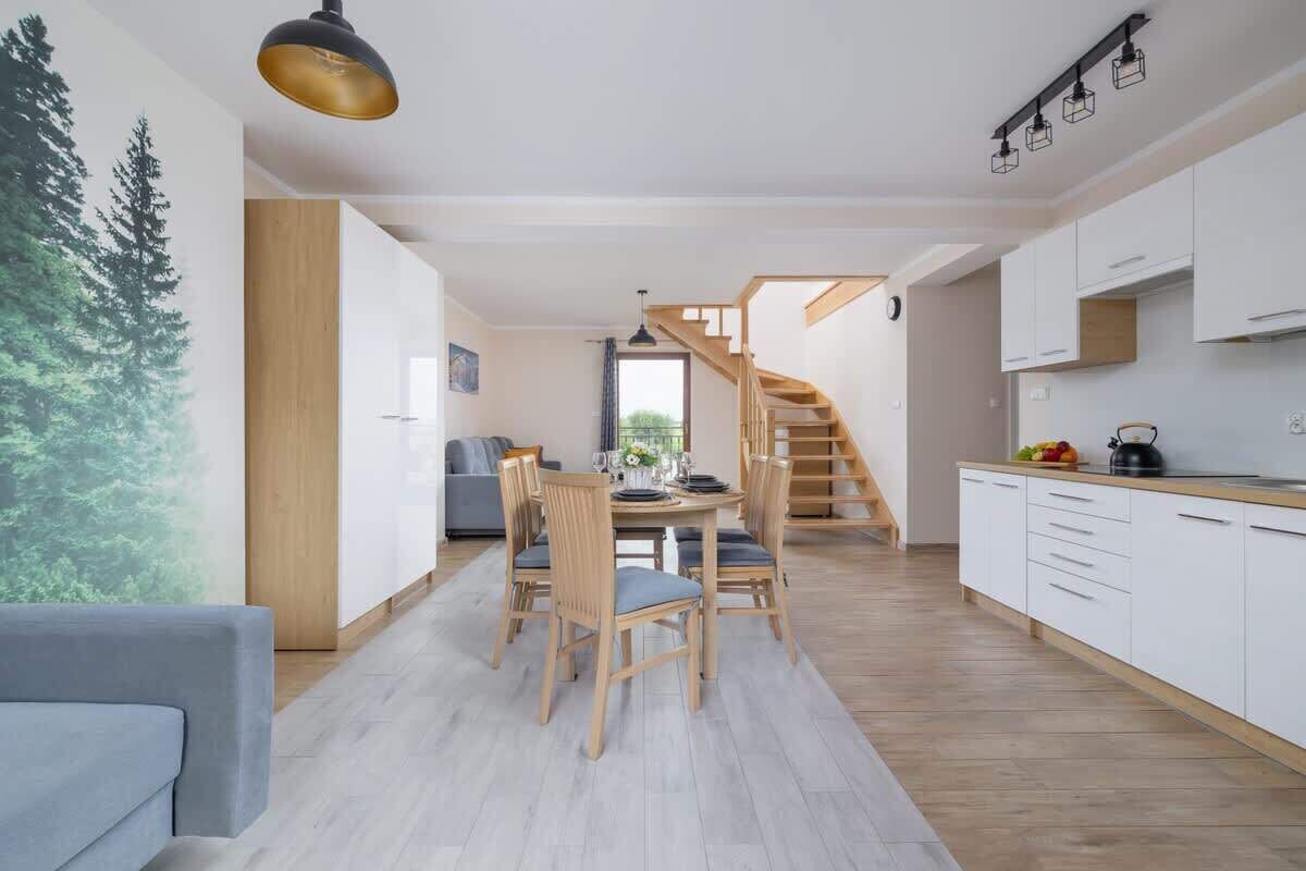 Una cocina moderna con armarios blancos, una escalera de madera y un comedor con mesa y sillas.