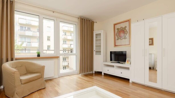 A modern living room with a beige sofa, a glass coffee table, a flat-screen TV, and a wardrobe.