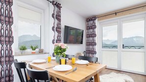 A dining area with a wooden table set for four, black chairs, a vase with flowers, and a view of mountains through large windows. - Cozy Apartment | With Mountain View and Balcony (Koscielisko)