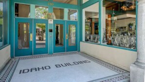 Entrada de um edifício com portas e janelas azuis-esverdeadas, o número "280" acima das portas e um tapete de entrada com a inscrição "Idaho Building".