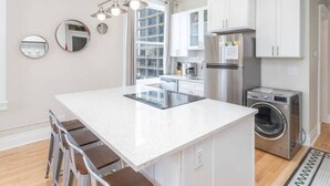 Uma cozinha moderna com armários brancos, uma ilha central, eletrodomésticos de aço inoxidável e máquina de lavar e secadora embutidas.
