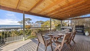 Une terrasse en bois avec une table dressée pour le repas, un barbecue et une vue sur la mer.